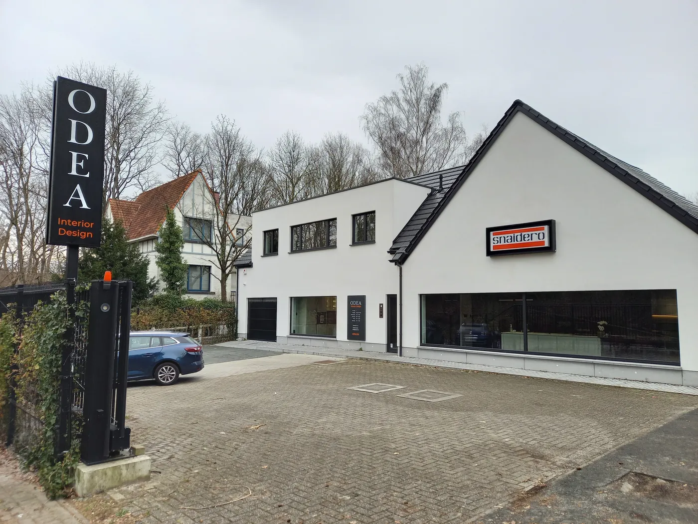 De showroom van ODEA Interior in Beersel vanaf de straat: wit gebouw met puntgevel, ODEA-zuil en parking voor de ingang